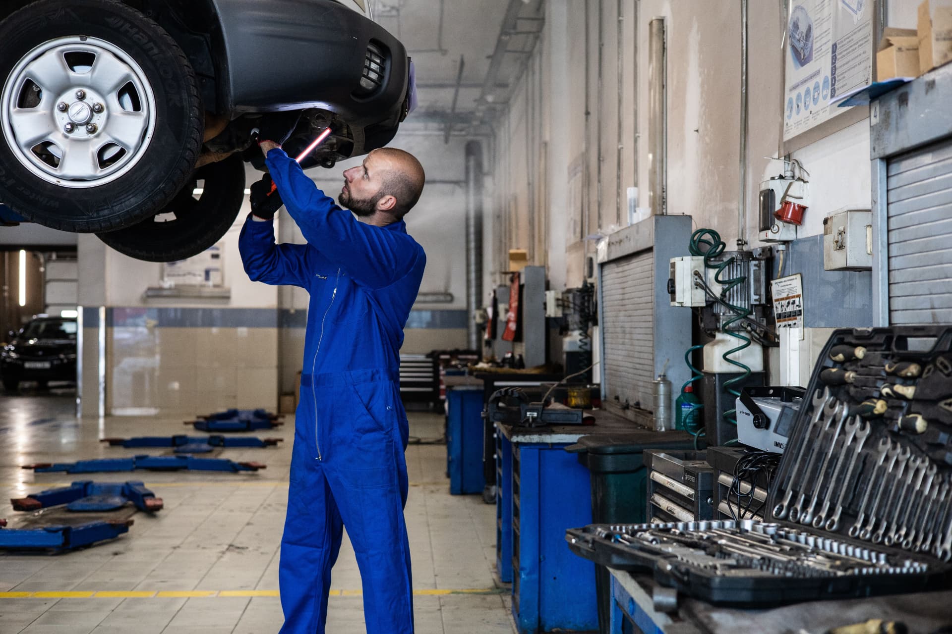 Rental car fleet preventive maintenance in a service garage Mechanic inspecting car undercarriage in rental fleet service bay