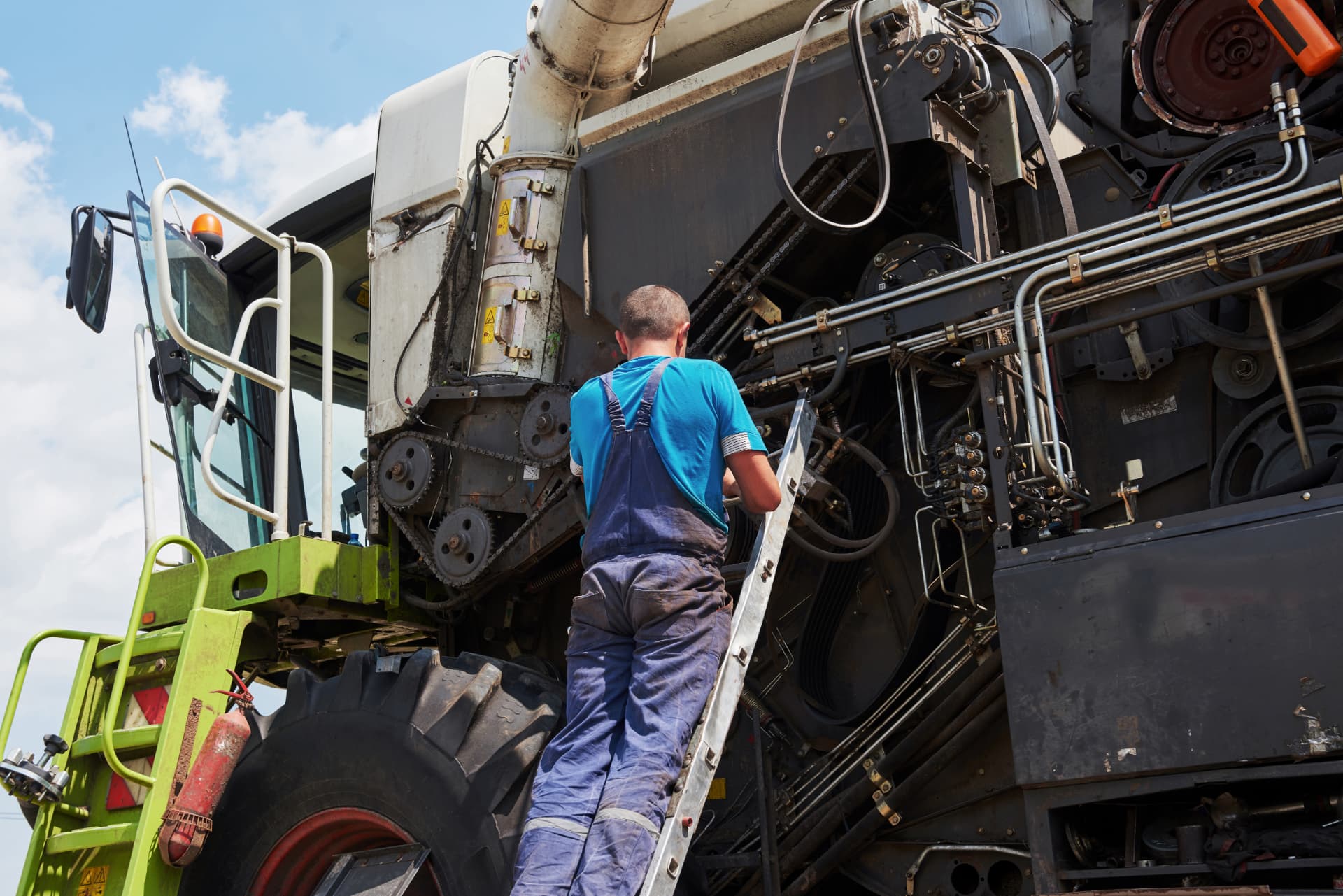 Pre-season maintenance on farm combine harvester equipment Farm technician on a ladder servicing a combine harvester before planting season